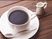 テーブルの上に置かれた白いカップにはコーヒーが入っていて、横にはミルクが添えられている