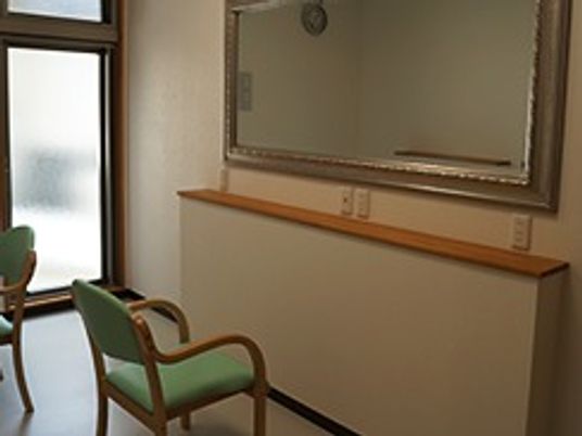 理美容室にはシンプルな大きな鏡が壁にかけられ、その前に緑色のいすが置かれている。