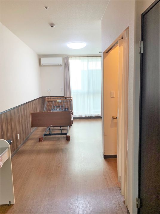 介護用ベッドがある小さな部屋の様子。手前にトイレや洗面台など水回りがある