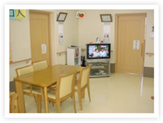 木製のダイニングテーブルやテレビが置かれ、居室のドアもすぐそばに設置されている。