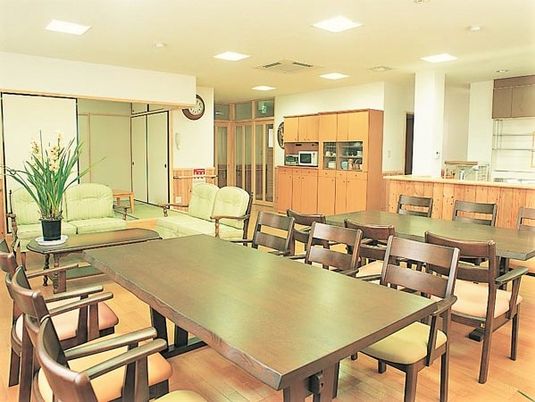 大きめサイズのテーブルと椅子が並ぶ施設内の共有スペース。奥のほうに畳のこ上りがある