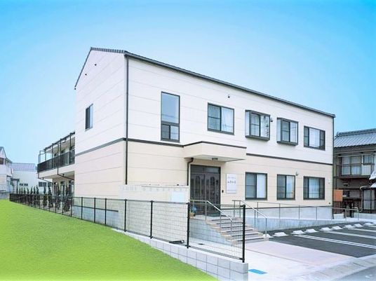 ２階建てのグループホームの外観。手前に駐車場が数台分用意してある様子