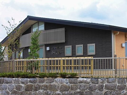 オレンジとダークブラウンの外壁の平屋建ての建物は石垣の上にあり、草木が植えられている。