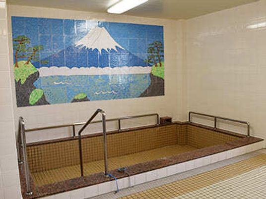 富士山の絵が書かれた壁がある、大浴室内の様子。プールのような形の浴槽