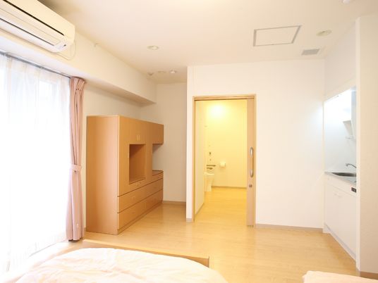 居室は広く大きな収納棚やキッチン、トイレなどが付いている。手前にはベッドの足元の部分が見えている。