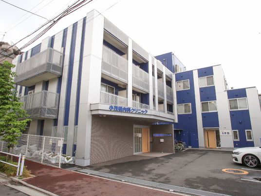 ３階建ての建物の外観。グレーとブルーのスタイリッシュな建物。左手前の建物にはクリニックの名前が書かれている。