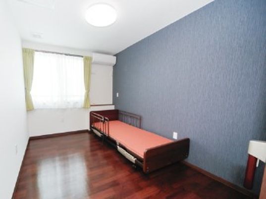 シックな色合いの壁民と小さなベッドが置いてある施設内の居室の様子