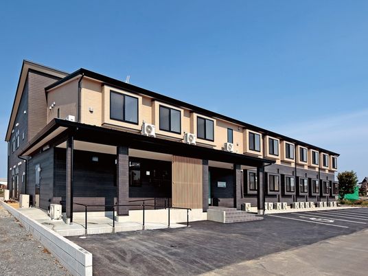２階建ての建物は日当たり良好で建物の前には駐車場があり、玄関先には手すり付きのスロープと階段がある。