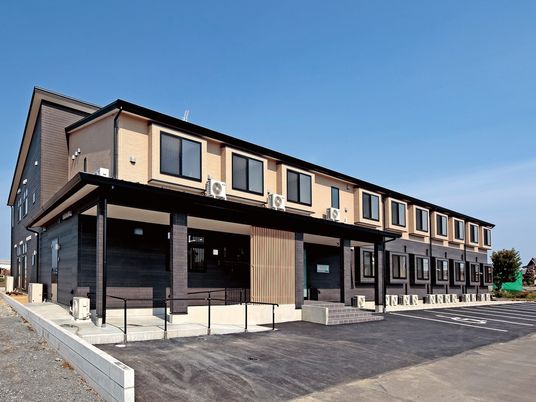 ２階建ての建物は日当たり良好で建物の前には駐車場があり、玄関先には手すり付きのスロープと階段がある。