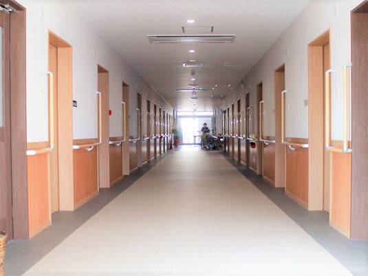 まっすぐに続く廊下の両側に個室のドアと手すりがある様子が映った写真