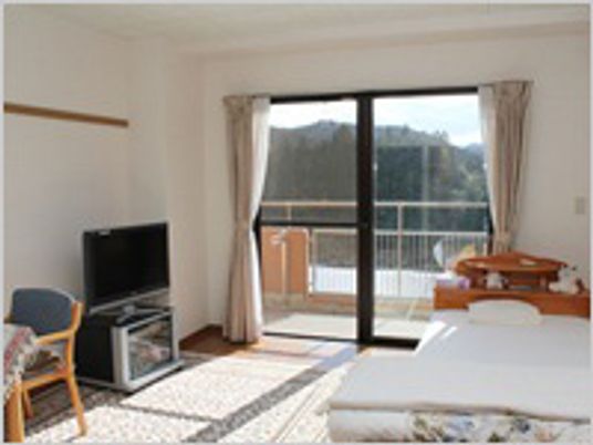 大きな窓の付いた部屋には寝具付きのベッドやテレビ、一人用の椅子が置かれている。