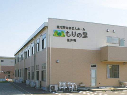白とベージュの2階建ての建物はエル字型で敷地内には広い駐車場があり、日当たりのいい場所に建っている。