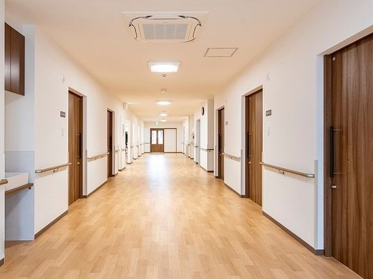 幅の広い廊下の両サイドには居室ドアや手すりが付き、突き当りにはドアがある。