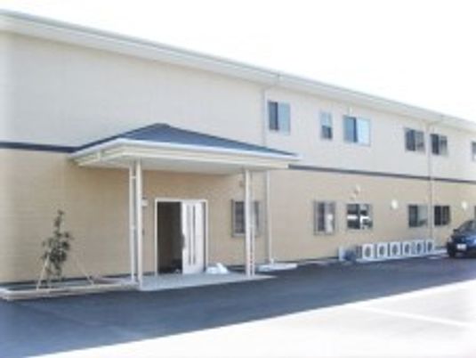 2階建ての建物はベージュ系で横に長く、玄関部分には屋根が付いている。