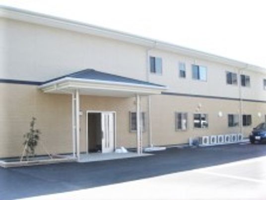2階建ての建物はベージュ系で横に長く、玄関部分には屋根が付いている。