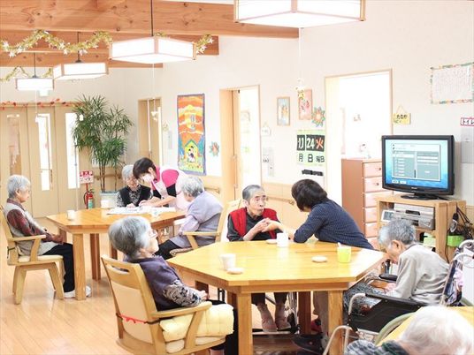 天井の高いリビングダイニングでくつろぐスタッフと入居者の様子。