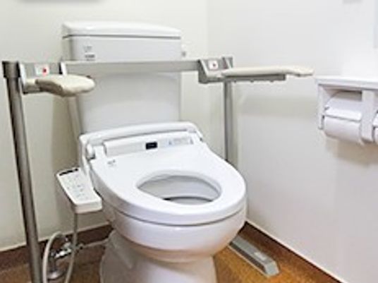 両側に手すりが付いている高齢者用のトイレ。ウォシュレット、トイレットペーパーなどが付いているトイレ