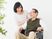 白いゆったりとした服を着た高齢女性と笑顔で話している眼鏡をかけた車いすの高齢男性。