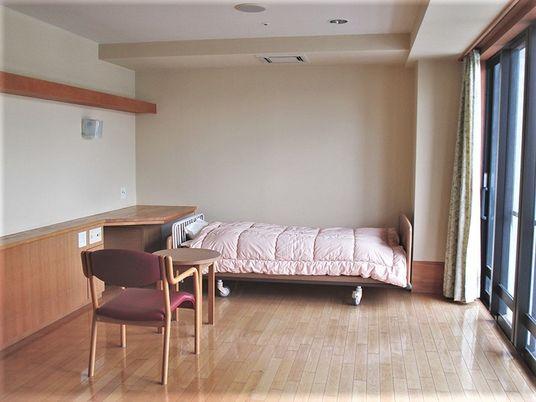 ベッドが一つだけ置いてある施設内の居室の様子。右側に窓があり日航が差し込んでいる