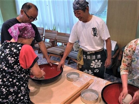 赤い大きな椀の中で蕎麦となる生地を丸めている入居者は、エプロンを付けている。