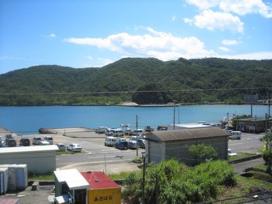 青空の下には山や海が広がり、港にはたくさんの車が止まっている。
