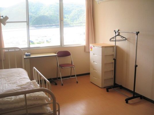 居室にはベッドや収納ケース、売プいすなどがあり、窓からは海や山が見える。