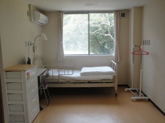 白いベッドにエアコン、白い収納エースなどが置かれ、窓からは明るい日差しが降り注いでいる。