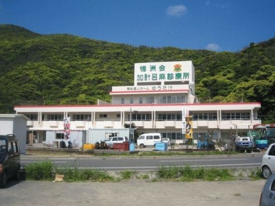 建物を少し遠くから見た風景。建物の後ろには青々とした山々が広がっている。