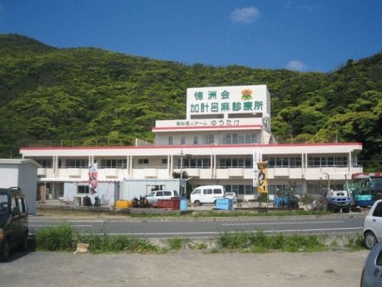 建物を少し遠くから見た風景。建物の後ろには青々とした山々が広がっている。