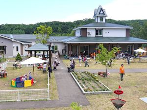 白とグリーンの建物を中心として、広い敷地内には花壇や広場があり、たくさんの子どもたちが遊んでいる。