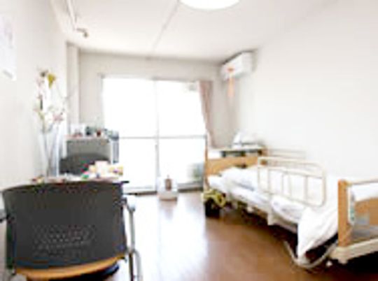 介護用ベッドとタンス、いすなどが置いてあるワンルームタイプの部屋の写真
