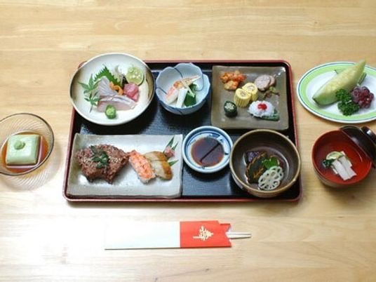 握り寿司や赤飯、刺身、前菜盛り合わせなどがあるテーブルにはメロンなどの果物もある。