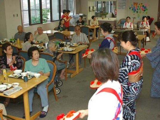 手作りの花笠を持って踊っている女性たちを見ている入居者たち。着物を着て踊っている人もいる。