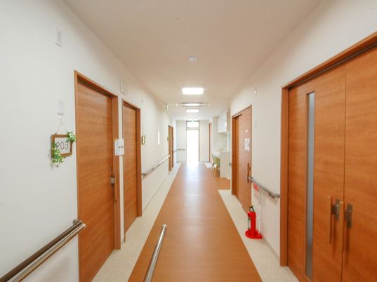 まっすぐな廊下。両サイドに居室のドアと手すりがあり、手前の居室のドアにはフェイクグリーンが飾られている。