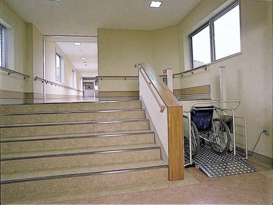 幅の広い階段の横に設置された昇降機には車いすが設置され、手すりが付いている。