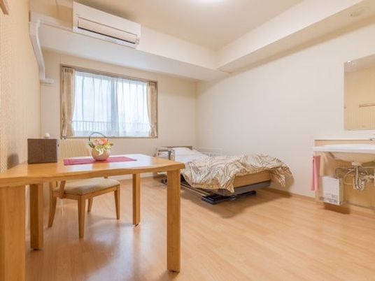 部屋の中を写した写真。エアコン、ベッド、いす、机、洗面台がある