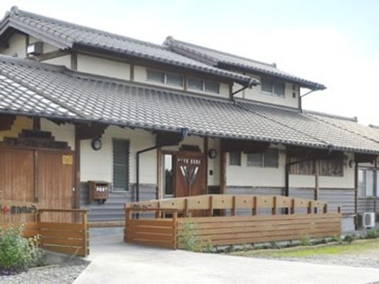 グレーの瓦屋根が付いた平屋建ての建物。平屋建ての建物は一部2階建てで庭もある。