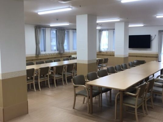 テレビが設置された食堂には大きな木製のダイニングテーブルセットが複数置かれている。