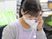 髪を後ろで一つに結び、薄紫色のエプロンとマスクを付けた女性スタッフが電話で応対をしている様子。後ろにはファイルが並んでいる。