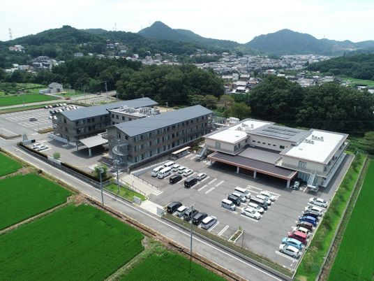 駐車場がある広い敷地内には白い2階建ての建物とがあり、左側にはグレーの3階建ての建物がある。3階建ての建物はエイチ型。