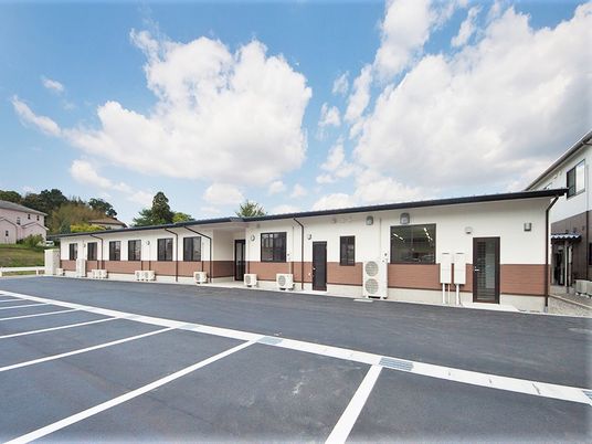 平屋建ての建物は緑に囲まれ、横に長い造り。近くに2階建ての建物もある。