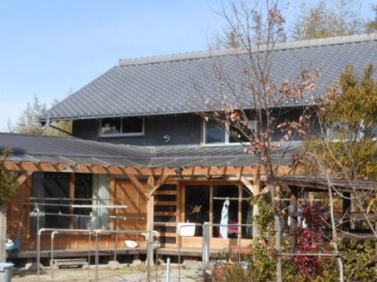グレーの瓦屋根が付いた２階建ての建物は日当たり良好で明るい雰囲気。庭には洗濯物干し場がある。