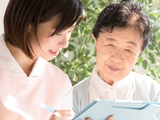 カルテのようなものを見ながら真剣な表情で話しているエプロンを付けた若い女性スタッフと高齢女性。