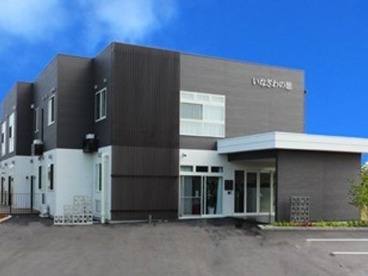 モノトーンの2階建ての建物には大きな駐車場が付き、車寄せの周りには花壇もある。