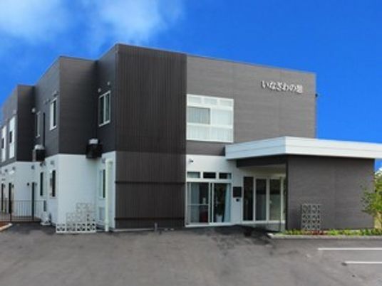 モノトーンの2階建ての建物には大きな駐車場が付き、車寄せの周りには花壇もある。
