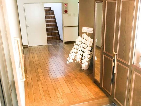 お祝いの花が飾られている玄関には大きな靴箱があり、手すりも付いている。正面には階段も付いている。