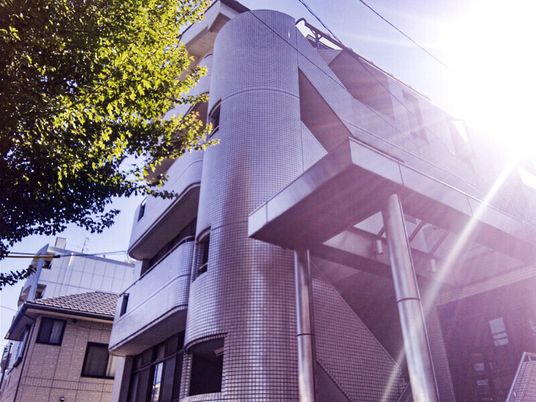 日当たりのいい場所に建っているグレー系の外観の大きな建物。建物の前には大きな木がある。