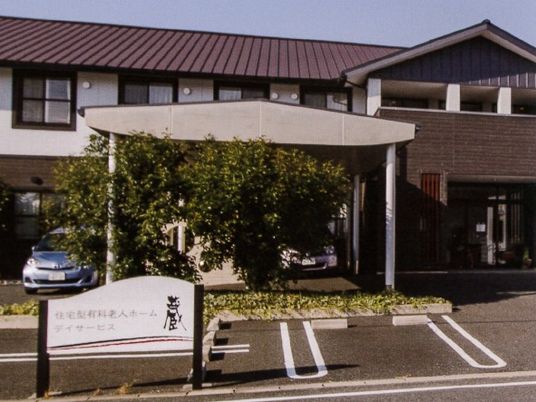 2階建ての施設の外観。雨除けのひさしと駐車場、個室が並んでいる様子が分かる