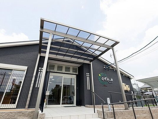 ダークグレーの平屋建ての建物は日当たりのいい場所に建っていて、玄関先には手すり付きのスロープと階段がある。