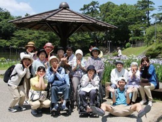高齢者が集まって外出先で記念写真を撮っている様子。施設のレクリエーション時の写真